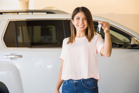 Cute young woman holding the keys for her brand new car at a dealershipの写真素材