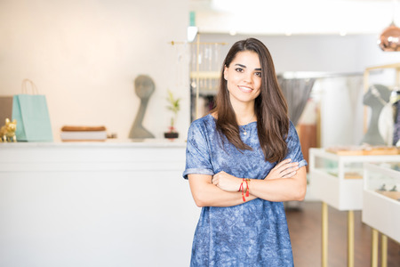 Cute female Latin business owner with her arms crossed standing in a jewelry and fashion shopの写真素材