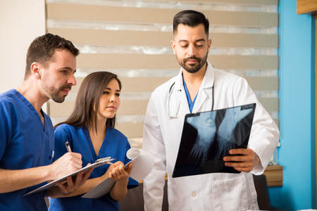 Young doctor and medical residents analyzing x-rays of a patient in a hospital room