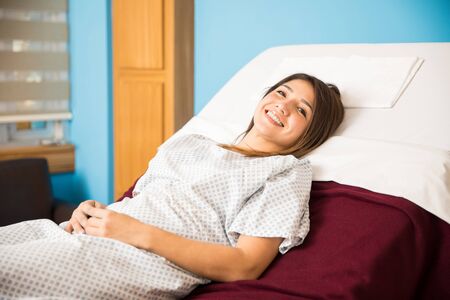 Portrait of a beautiful young Hispanic woman lying on a hospital bed and smiling during her recoveryの写真素材