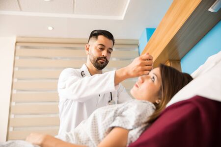 Low angle view of a handsome Hispanic doctor with a beard using an otoscope to examine a patientの写真素材