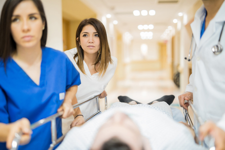 Group of health professionals using a gurney to transport a male patient to an operating room during an emergencyの写真素材