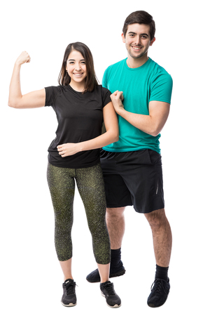 Full length view of a young Hispanic couple in sporty outfit showing their arm strength and smilingの写真素材