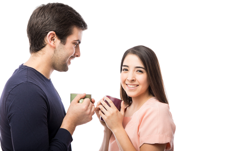 Beautiful young brunette enjoying a cup of coffee with her boyfriend and smiling in a studioの写真素材