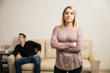 Portrait of a young woman looking serious and upset with her arms crossed while her boyfriend lays in the backの写真素材