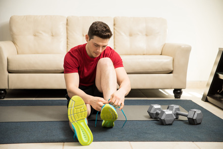 Good looking young man tying his shoes and getting ready to exercise at homeの写真素材