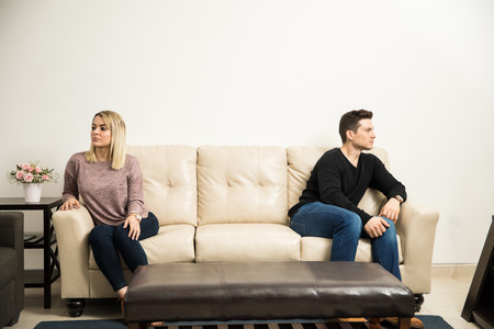 Wide view of a young couple sitting on opposite sides of a couch, after having a fight and some problemsの写真素材
