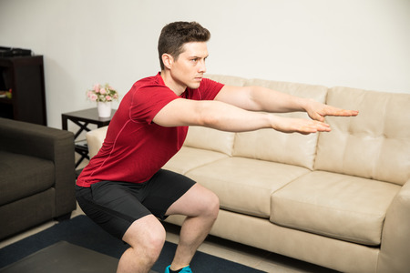 Portrait of a handsome athletic young man working out and doing squats in the living room