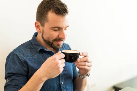 Handsome young man smelling a cup of coffee and enjoying the aromaの写真素材