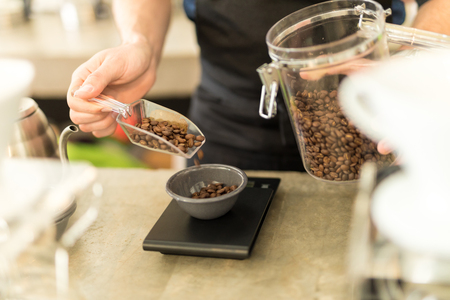 Closeup of a male barista pouring coffee grains on a scale before brewing some coffee in a cafeの写真素材