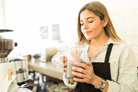 Cute young female barista smelling some coffee grains and enjoying her job at a coffee shopの写真素材