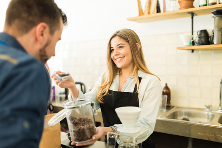 Cute female barista giving coffee grains to smell to a customer in a coffee shop