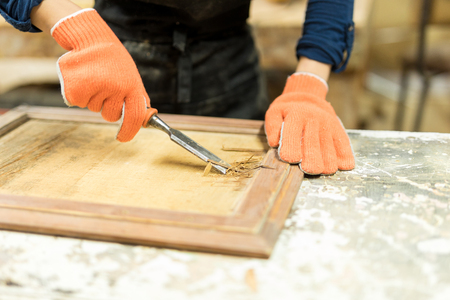 Closeup of a female carpenter doing some wood carving using a gouge in a workshop