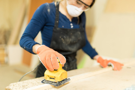 Closeup of a pretty young female carpenter using an electric sander to work on some wood in a workshopの写真素材