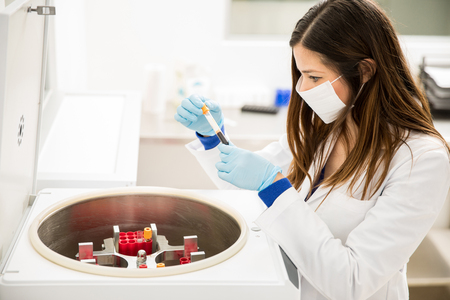 High angle view of a beautiful female chemist looking at some blood samples out of a centrifuge in a laboratoryの写真素材