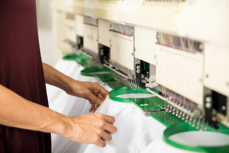 Closeup of a woman placing several garments on an embroidery machine in a textile factoryの写真素材