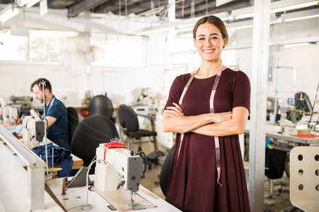 Portrait of a beautiful seamstress carrying a tape measure and working in a textile factoryの写真素材