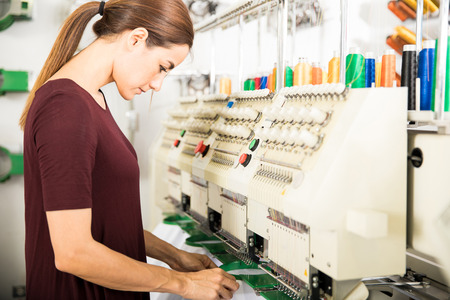 Profile view of a woman putting many garments in place in an embroidery machine at a factory