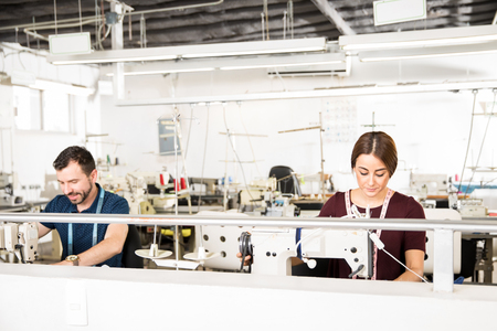 Wide view of a couple of tailors using sewing machines for work in a textile factoryの写真素材