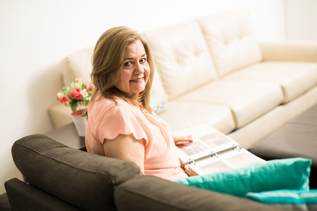 Attractive aged grandmother proud of her past life sitting on the sofa in the living roomの写真素材