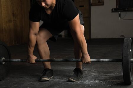 Closeup of a strong young man doing a barbell deadlift in a cross-training gymの写真素材