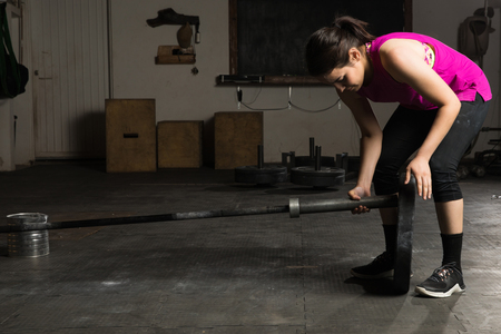 Active young woman setting up a barbell with some weights before working out in a gymの写真素材