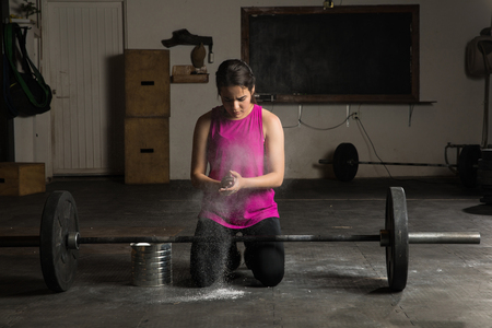 Active young woman using gym chalk to improver her grip before lifting a barbell at the gymの写真素材