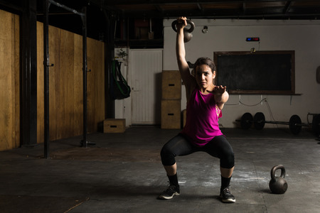 Full length view of a pretty young fit woman doing kettlebell swings in a gymの写真素材
