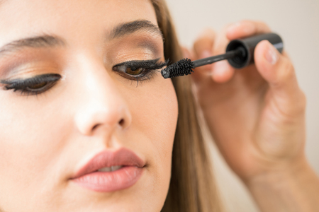 Good looking young woman getting some mascara on her eyelashes by her makeup artist, seen up close