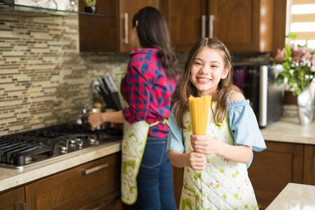 Portrait of a cute Latin girl about to make some pasta at home with her motherの写真素材