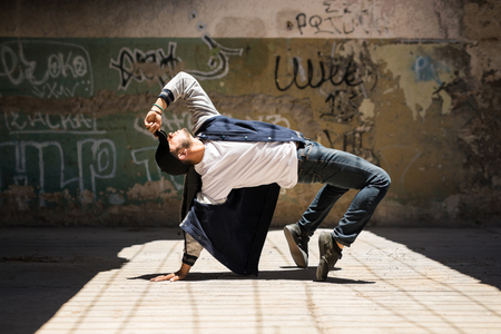 Young male hip hop dancer arching back and showing some of his dance moves in an urban setting with graffiti wallsの写真素材