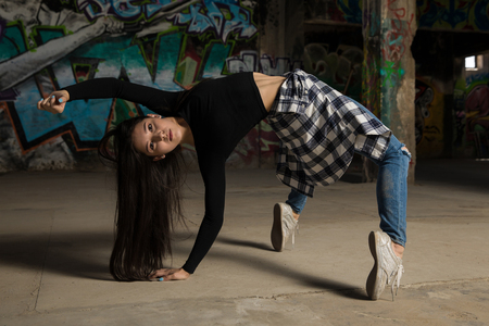 Portrait of a pretty female dancer bending backwards and standing on her toes in front of a graffiti wallの写真素材
