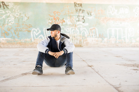 Good looking male urban dancer sitting outdoors in an urban setting with graffiti walls. Lots of copy spaceの写真素材