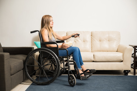 Full length view of a young woman on a wheelchair watching TV to pass the time