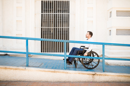 Profile view of a good looking young man going up a building ramp on a wheelchairの写真素材