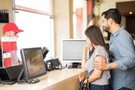Profile view of a young couple buying movie tickets and looking at a screen while deciding what to...