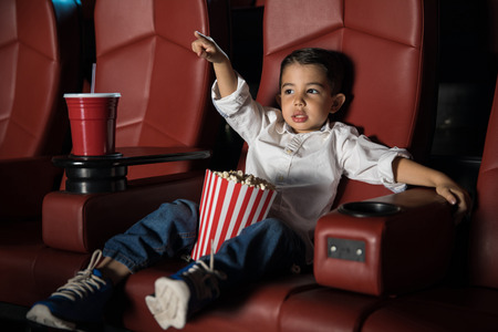 Portrait of a little Latin kid watching a movie and pointing at the screen in a cinema theaterの写真素材