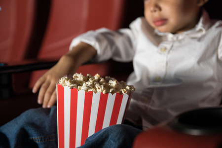 Closeup of a little boy sitting in a movie theater and enjoying a movie while eating popcornの写真素材
