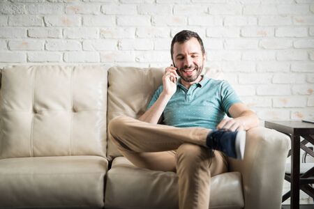 Young man talking on the phone with a good old friend sitting on a couch in the living room