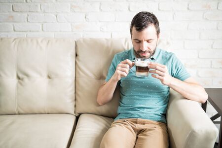 Young Hispanic man having a relaxing afternoon at home enjoying a cappuccinoの写真素材