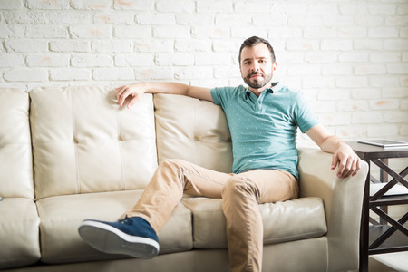 Handsome man on his 30s wearing casual clothes relaxing on a couch in the living roomの写真素材