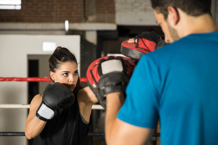 Portrait of a beautiful young woman training with her coach with boxing mitts in a boxing gymの写真素材