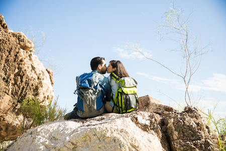 Happy couple of hikers sharing a cute kiss sitting on a rock at the top of the mountainの写真素材