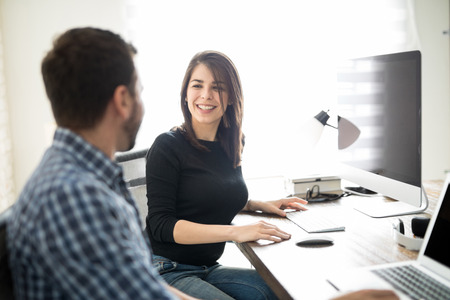 Happy Hispanic woman smiling at a coworker while they talk about work at the officeの写真素材