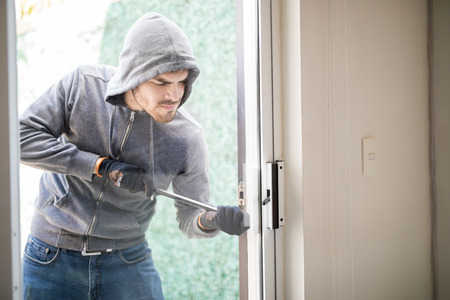 Male burglar wearing a hoodie forcing entry into a house with a plank through a back doorの写真素材