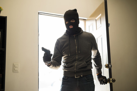 Burglar with a gun and a ski mask on the front door of a house before robbing itの写真素材