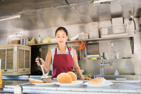 Attractive young woman with an apron working in a food truck and preparing a few burgers
