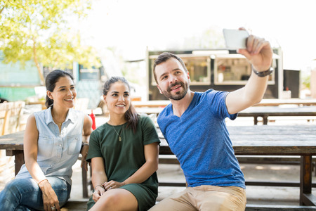 Group of three friends sitting on a table and taking a selfie while having a good time togetherの写真素材