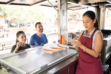 Attractive female food truck cook taking orders from her customers and selling hot dogs