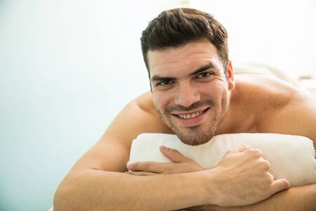 Portrait of an attractive young Hispanic man lying on a bed in a spa and smilingの写真素材